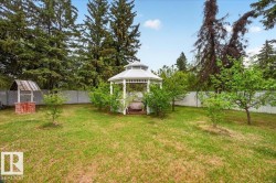 Expansive backyard featuring a white gazebo, a decorative well with a brick base, and mature perimeter trees - 