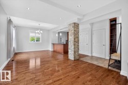 Spacious room featuring wood-finish flooring, a stone-clad structural column, recessed lighting, and a chandelier - 