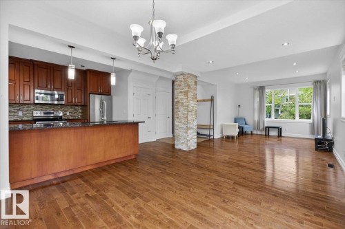 Open-concept living space with wood-finish flooring, a kitchen island with dark stone countertops, stainless steel appliances, and a stone-clad pillar - 10958 88 Avenue, Edmonton, AB 