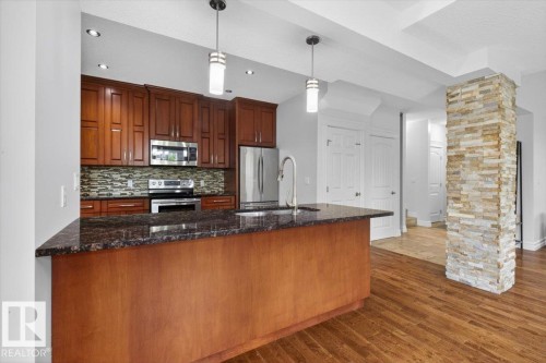 Kitchen featuring a large island with a dark countertop, rich wood cabinetry, stainless steel appliances, a mosaic tile backsplash, and recessed lighting - 10958 88 Avenue, Edmonton, AB 