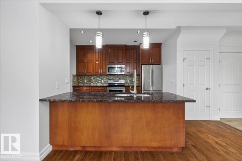 Kitchen featuring a central island with a stone countertop, rich wood cabinetry, stainless steel appliances, and a tiled backsplash - 10958 88 Avenue, Edmonton, AB 
