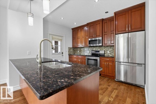 Kitchen island with dark speckled countertop and undermount double basin sink, brushed nickel gooseneck faucet, and two pendant lights - 10958 88 Avenue, Edmonton, AB 