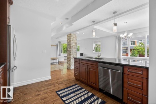 Kitchen featuring wood-finish flooring, dark wood cabinetry, a dark countertop, a stainless steel dishwasher, and a stainless steel refrigerator - 10958 88 Avenue, Edmonton, AB 