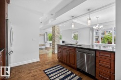 Kitchen featuring wood-finish flooring, dark wood cabinetry, a dark countertop, a stainless steel dishwasher, and a stainless steel refrigerator - 