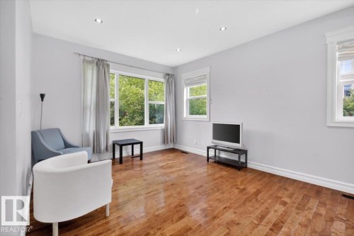 Spacious room featuring wood-finish flooring, recessed ceiling lighting, multiple windows with white trim, and light gray wall finishes - 10958 88 Avenue, Edmonton, AB 