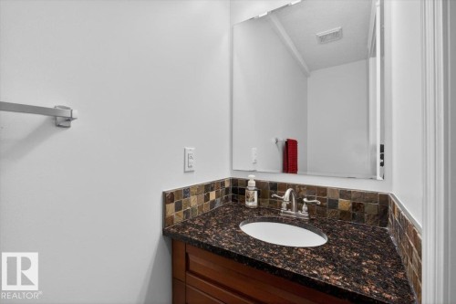 Vanity area featuring a dark stone countertop with an integrated oval sink, a mosaic tile backsplash, and a wood-finish vanity cabinet - 10958 88 Avenue, Edmonton, AB 