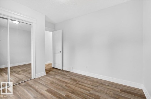 Spacious interior featuring wood-finish flooring, mirrored closet doors, a white paneled door, and neutral painted walls - 10958 88 Avenue, Edmonton, AB 