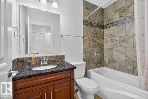 Bathroom featuring a dark wood-finish vanity with an undermount sink, a dark speckled countertop, and a tiled backsplash - 10958 88 Avenue, Edmonton, AB 