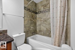 Bathroom featuring a bathtub with a tiled surround, a mosaic accent band, and a shower head with an arched shower rod - 