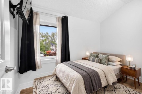 Bright bedroom featuring a large window with natural light, wood-finish flooring, white painted walls, and a textured ceiling - 10958 88 Avenue, Edmonton, AB 