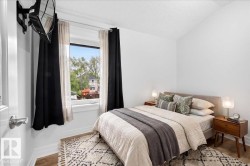 Bright bedroom featuring a large window with natural light, wood-finish flooring, white painted walls, and a textured ceiling - 