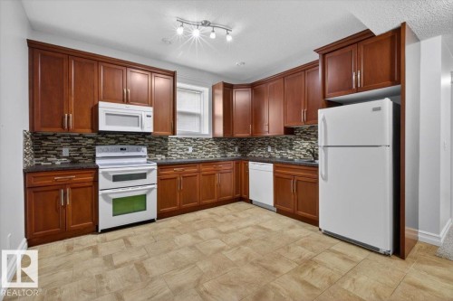 Kitchen featuring rich wood cabinetry, stone countertops, a mosaic tile backsplash, and light-toned tile flooring - 10958 88 Avenue, Edmonton, AB 