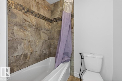 Bathtub and shower combination featuring extensive stone-look wall tiling with a mosaic accent band - 10958 88 Avenue, Edmonton, AB 