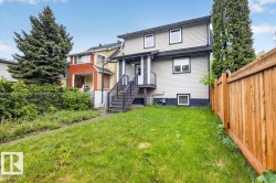 Rear exterior featuring light-colored siding, contrasting trim, a wood privacy fence, and an exterior staircase with metal railings - 