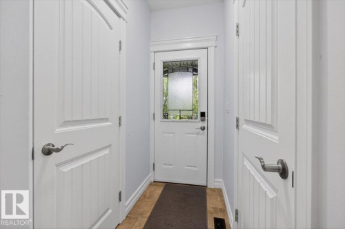 Entryway featuring a white paneled door with decorative glass, two white interior paneled doors, and wood-finish flooring - 10958 88 Avenue, Edmonton, AB 