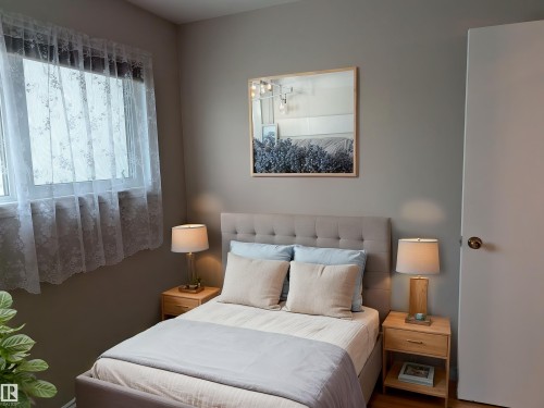 Bedroom featuring neutral wall tones, a window with lace curtains, and wood-finish flooring - 9443 75 Street, Edmonton, AB 