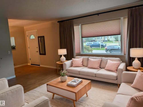 Living room featuring a large picture window with privacy blinds, wood-finish flooring, and a decorative entry door with an arched glass insert - 9443 75 Street, Edmonton, AB 