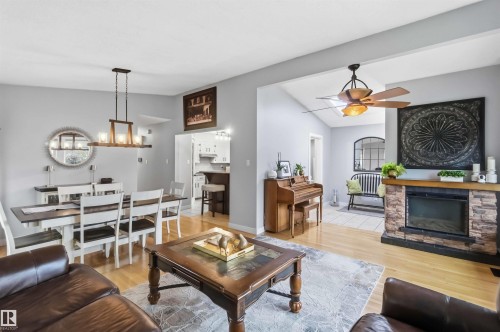 Open-concept living space with light-toned wood-finish flooring, a stone-front fireplace, and a vaulted ceiling - 11431 144 Avenue, Edmonton, AB 