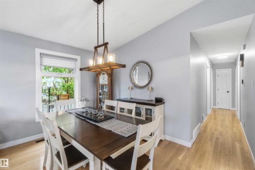 Dining area featuring light wood-finish flooring, a window with exterior tree views, and a contemporary chandelier - 11431 144 Avenue, Edmonton, AB 