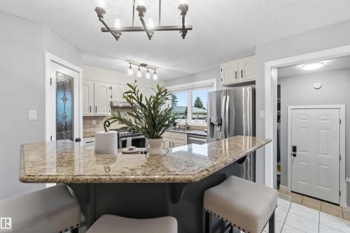 Kitchen featuring a granite-finish breakfast bar, stainless steel appliances, white cabinetry, and recessed lighting - 11431 144 Avenue, Edmonton, AB 