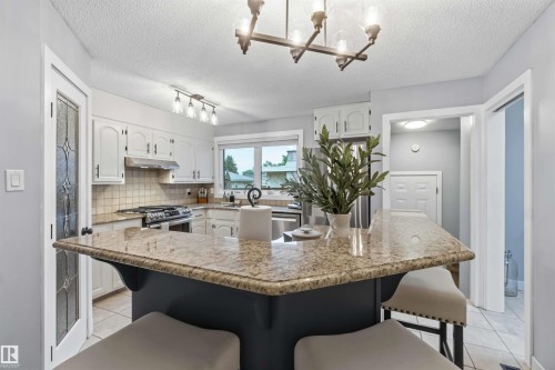 Kitchen featuring a spacious island with a light granite countertop, white cabinetry with dark hardware, a stainless steel range, and tile flooring - 11431 144 Avenue, Edmonton, AB 