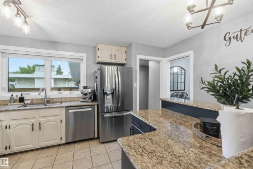 Kitchen featuring stainless steel appliances, speckled stone countertops, and light-toned cabinetry - 11431 144 Avenue, Edmonton, AB 