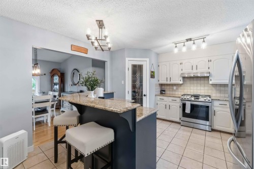 Kitchen featuring a central island with a granite countertop, white cabinetry with dark hardware, stainless steel appliances, and a tiled backsplash - 11431 144 Avenue, Edmonton, AB 