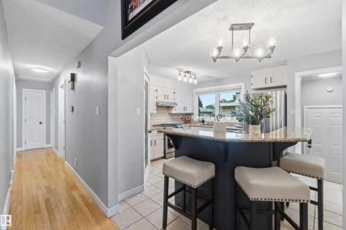 Kitchen island with a light-colored stone countertop, dark cabinetry, and integrated seating - 11431 144 Avenue, Edmonton, AB 