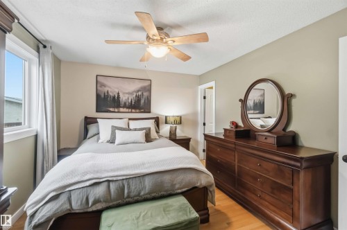 Bedroom featuring light wood-finish flooring, a contemporary ceiling fan with integrated lighting, and a large window with white trim - 11431 144 Avenue, Edmonton, AB 