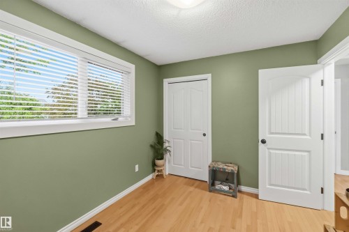 Interior room featuring wood-finish flooring, a white-framed window with horizontal blinds, and a white paneled door with black hardware - 11431 144 Avenue, Edmonton, AB 