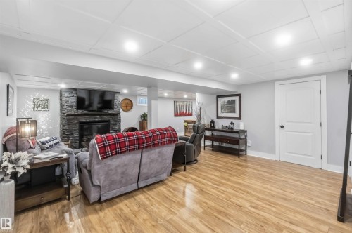 Spacious recreation room featuring wood-finish flooring, a stacked stone fireplace, and recessed lighting - 11431 144 Avenue, Edmonton, AB 