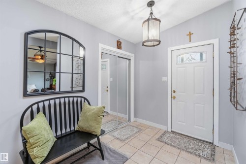 Foyer featuring tile flooring, a decorative entry door with an arched window insert, a built-in closet with mirrored sliding doors, and an overhead lantern light fixture - 11431 144 Avenue, Edmonton, AB 
