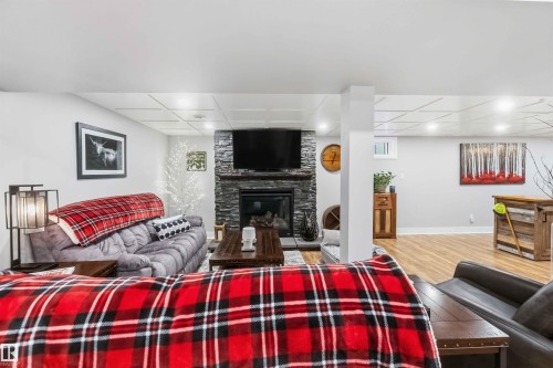 Living area featuring a stone-clad fireplace with an inset television, wood-finish flooring, recessed lighting, and a white grid ceiling - 11431 144 Avenue, Edmonton, AB 
