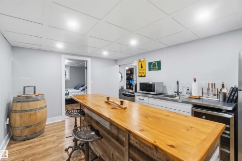 Custom bar featuring a wood-finish countertop and paneling, stainless steel sink, and built-in beverage refrigerator - 11431 144 Avenue, Edmonton, AB 