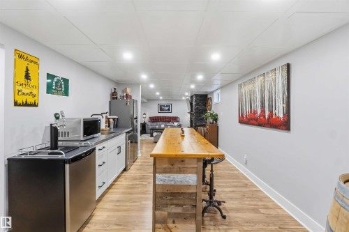 Finished basement featuring wood-finish flooring, recessed lighting, and a built-in wet bar with white cabinetry and a stainless steel countertop - 11431 144 Avenue, Edmonton, AB 