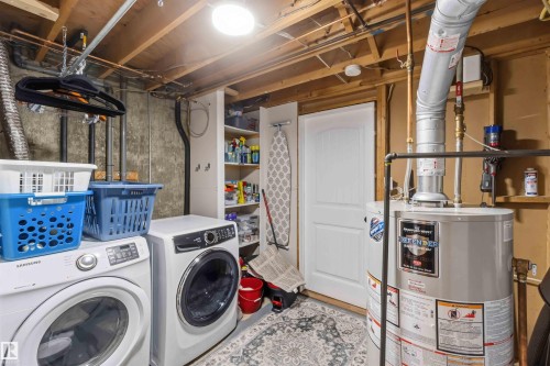 Dedicated laundry area featuring a washer and dryer, built-in shelving, a water heater, and a white paneled door - 11431 144 Avenue, Edmonton, AB 