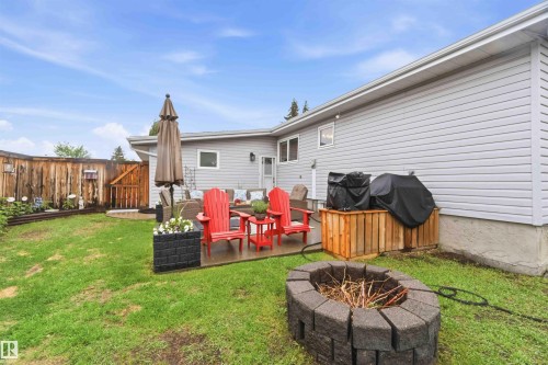 Expansive backyard featuring a concrete patio, wooden privacy fence, a fire pit with block pavers, a grass lawn, and siding exterior - 11431 144 Avenue, Edmonton, AB 