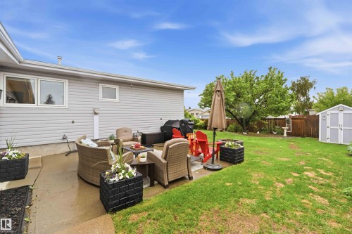 Expansive backyard featuring a concrete patio, a detached storage shed, and a mature tree - 11431 144 Avenue, Edmonton, AB 