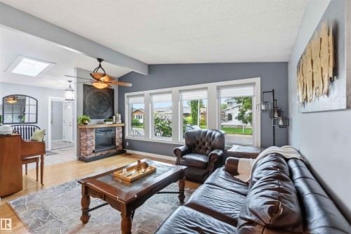 Living area featuring light wood-finish flooring, a stone-clad fireplace with a wood mantle, and a ceiling fan with integrated lighting - 11431 144 Avenue, Edmonton, AB 