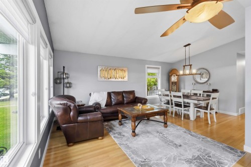 Open-concept living and dining area featuring light wood-finish flooring, a contemporary ceiling fan, and a linear chandelier over the dining space - 11431 144 Avenue, Edmonton, AB 
