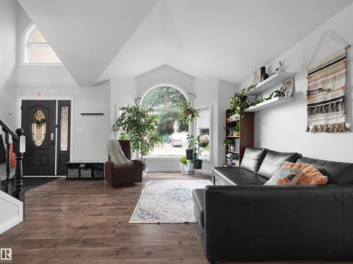 Open-concept living space featuring wood-finish flooring, a vaulted ceiling, and a large arched window - 208 Ferguson Place, Edmonton, AB 