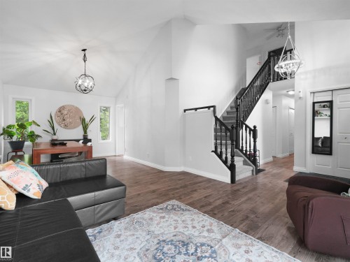 Vaulted ceilings featuring a contemporary chandelier, wood-finish flooring, and a multi-level staircase with dark wood banisters - 208 Ferguson Place, Edmonton, AB 