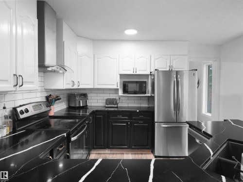 Kitchen featuring black countertops with white veining, white upper cabinetry, and contrasting black lower cabinetry - 208 Ferguson Place, Edmonton, AB 