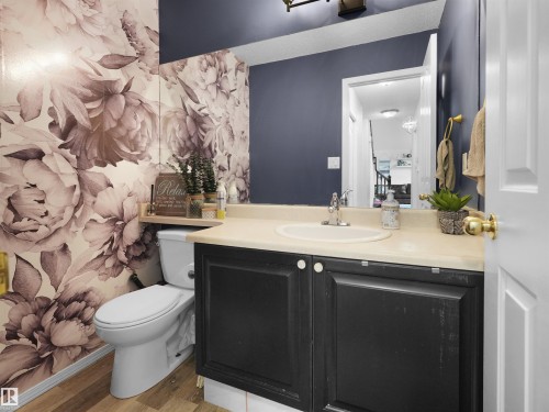 Powder room featuring a floral accent wall, dark vanity with light-colored countertop, and a white toilet - 208 Ferguson Place, Edmonton, AB 