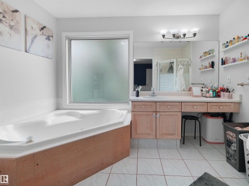 Soaking tub with a wood-finish surround, complemented by a large frosted window - 208 Ferguson Place, Edmonton, AB 
