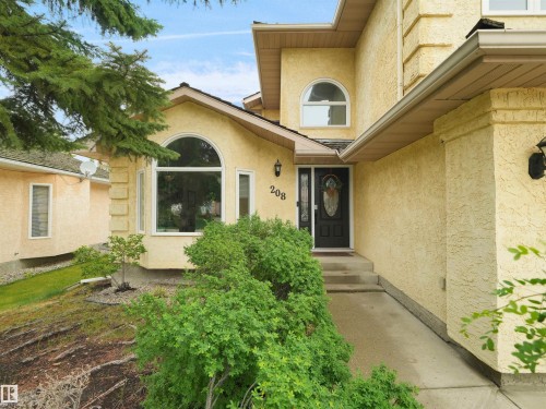 Stucco exterior featuring an arched bay window and a decorative glass entry door - 208 Ferguson Place, Edmonton, AB 