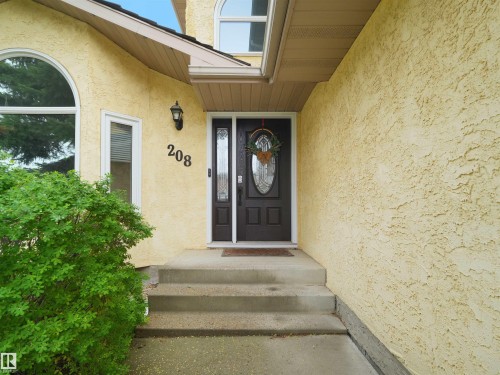 Inviting entryway featuring a dark wood-finish door with decorative glass inserts, a complementary sidelight, and an exterior wall light fixture - 208 Ferguson Place, Edmonton, AB 