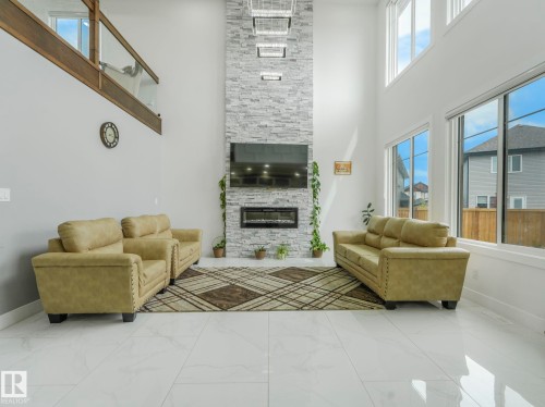 Living area featuring a floor-to-ceiling stone-faced fireplace with an electric insert, a mounted television, and high ceilings - 3101 Pelerin Crescent, Beaumont, AB 