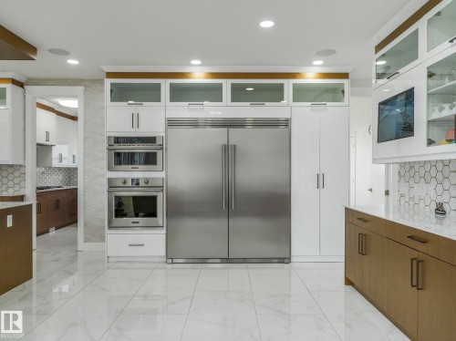 Gourmet kitchen featuring a built-in stainless steel refrigerator, double ovens, white and wood-finish cabinetry, honeycomb tile backsplash, and large format white tile flooring - 3101 Pelerin Crescent, Beaumont, AB 