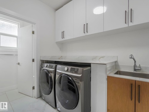 Dedicated laundry area featuring a stainless steel sink, wood-finish cabinetry, and marble-look countertops - 3101 Pelerin Crescent, Beaumont, AB 